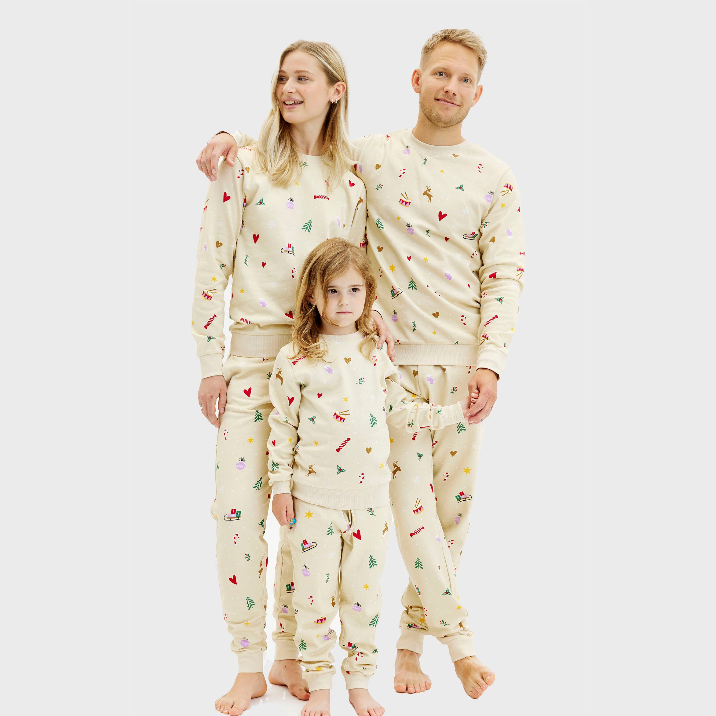 Beiges Weihnachtspyjama Set aus Sweatstoff für Damen, Herren und Kinder mit buntem Weihnachtsmuster.